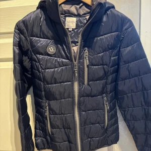 Uhip stall jacka - Snygg jacka från Uhip. Jackan har flera dragkedjefickor, ribbade muddar med tumhål och en logga på bröstet. Perfekt för kyliga dagar när du vill hålla stilen och värmen.