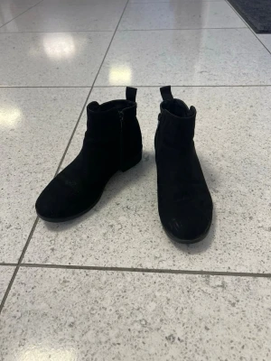 Svarta mocka boots med dragkedja - Snygga svarta boots i mocka med rund tå och platt sula. De har praktisk dragkedja på sidan och en enkel, stilren design som passar till många outfits. Perfekta för höst och vinter när du vill ha en clean look.