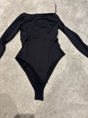 Svart långärmad bodysuit från H&M XS - Säljer en svart långärmad bodysuit från H&M i storlek XS. Använd MAX 3 gånger då jag tänkte köpa en annan body. Modellen har en asymmetrisk offshoulder-design med en axel bar och en smal passform. Materialet är mjukt och stretchigt, perfekt för att skapa en clean och snygg look. 