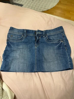 Lågmidjad jeanskjol - Säljer en blå jeanskjol från Esprit med klassisk femficksdesign och snygga broderade detaljer på bakfickorna. Kjolen är kort och har bälteshällor, knapp och dragkedja framtill. Perfekt för dig som gillar streetstyle och denim. Den är uppsydd för att vara kortare🩷