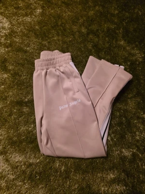  Palm Angels byxor beige  - S/M beige byxor från Palm Angels med vit logga på framsidan och vita sidoremsor med svart detalj.  Byxorna är knappt använda pga för stora. Qr coden funkar som den ska såklart. Äkta!