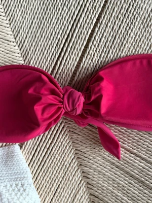 Rosa Bikinitopp med knyte - Rosa Bikinitopp med knyte, tillverkad i mjukt syntetmaterial. Toppen har en enkel design utan mönster och är formad med två breda partier som knyts ihop i mitten. .