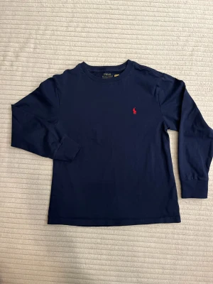 Mörkblå långärmad t-shirt Polo Ralph Lauren, strl 150 - Snygg mörkblå långärmad t-shirt från Polo Ralph Lauren med klassisk röd broderad logga på bröstet. Använd men välbehållen.