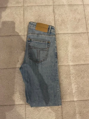 Blå jeans från Tiger of Sweden - Snygga blå jeans från Tiger of Sweden med klassisk femficksdesign och bruna sömmar. Jeansen har dragkedja i gylfen och bälteshällor. Materialet är slitstarkt denim och passformen är rak och normal. Perfekt för dig som gillar stilrena och tidlösa jeans.