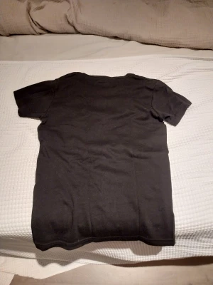 Supreme svart t-shirt med Bugs Bunny - Supreme t-shirt i svart med korta ärmar och tryck framtill av Bugs Bunny som kastar pengar. Supreme-loggan i rött och vitt syns tydligt. T-shirten är gjord i mjuk bomull och har en klassisk rund hals. Perfekt för dig som gillar streetwear och Looney Tunes.