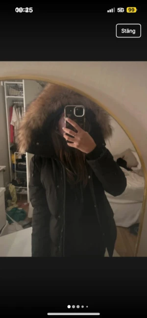 Svart pufferjacka med päls från Hollies - Säljer en svart pufferjacka frånHollies med stor fluffig fuskpäls på huvan. Jackan har dragkedja och knappar framtill, samt Hollies-logga på ärmen. Perfekt för kalla dagar och riktigt snygg passform.