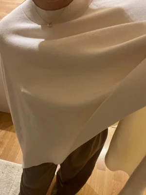 Vit poncho-tröja från Gina Tricot - Säljer en vit poncho från Gina Tricot i storlek S/M. Tröjan har en rund halsringning och är tillverkad i ett mjukt stickat material. Den har en loose passform och faller snyggt över axlarna, perfekt för lager-på-lager under hösten och vintern🤗Endast använd ett fåtal gånger så den är i toppen bra skick!