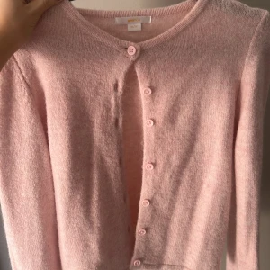 Ljusrosa kofta från Gina Tricot -  146-152 men passar xs-S Supermjuk ljusrosa kofta från Gina Tricot med rund hals och knappar framtill. Koftan är stickad och har långa ärmar, perfekt för att ge en söt och chill vibe till din outfit. Passar dig som gillar mjuka och fluffiga plagg i en feminin ton.