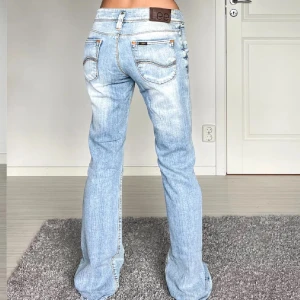 Ljusblå bootcut jeans från Lee - Snygga ljusblå jeans från Lee med bootcut passform och låg midja. Jeansen har slitna detaljer, klassiska fickor och Lee-lapp bak i midjan. Tillverkade i mjukt denimtyg som ger en avslappnad vibe.