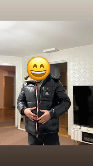 Svart Moncler pufferjacka med huva - Säljer en svart pufferjacka från Moncler med glansig finish, huva och klassisk logga på bröstet. Jackan har en rödvit randig dragkedja framtill och flera fickor. Perfekt för kalla dagar och riktigt snygg streetstil.