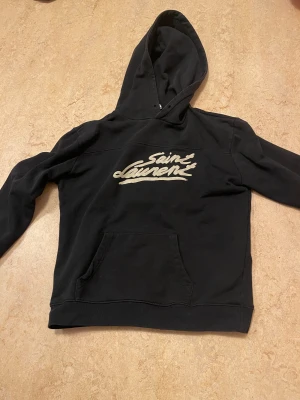 Svart saint Lauren hoodie med vit text - Hej! Säljer en sjukt snygg saint Lauren hoodie med vit text. Du får denna för ett väldigt bra pris! Bara 1100 för denna otroligt snygga hoodie! Kontakta vid frågor! Den har inga defekter på sig använd fåtal gånger!