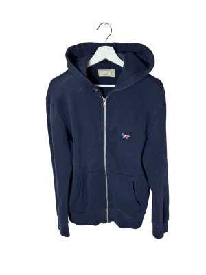Maison Kitsuné hoodie - Schysst mörkblå hoodie från Maison Kitsuné. Dragkedja framtill, två fickor och luva baktill. Hoodien är använd men fortfarande i bra skick.        Hör av dig vid frågor och funderingar!