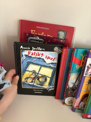 Falskt spel - En spännande bok med färgstarka illustrationer där två nyfikna barn kikar ut genom ett frostigt fönster. Perfekt för dig som gillar mysterier och äventyr! Passar unga läsare som vill ha en rolig och lite klurig berättelse.