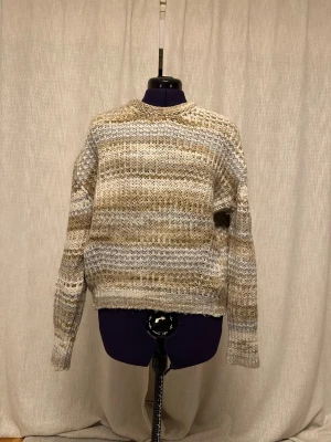 Beige stickad tröja från JJXX - Säljer en mysig stickad tröja från JJXX i storlek S. Tröjan har ett grovt, ribbat mönster och är randig i olika nyanser av beige och grått. Den har långärmad passform och rund hals. Perfekt för dig som gillar chill och stilren vibe.