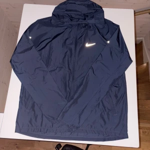 Nike Miller jacka💙 - 🔥 NIKE Vindjacka – Stilren, lätt & perfekt för alla årstider! 🔥 Säljer denna sjukt snygga och nästan helt oanvända Nike-vindjacka i en mörk, exklusiv blå ton. Den är både lätt, slitstark och vattenavvisande – perfekt för promenader, löpning eller bara som ett riktigt clean vardagsplagg. ✨ Reflekterande detaljer på bröstet och armen gör den extra snygg och synlig i mörker. ✨ Skön passform med huva och dragkedja hela vägen. 📌 Skick: Nästan ny – inga märken, inga defekter. 💥 Först till kvarn ‼️