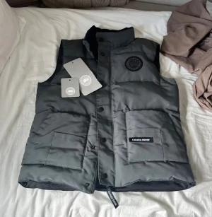 Canada goose väst - En canada goose väst i bra skick. Storlek Small men passar M bra.Säljs pga ingen användning. Ända defekten på den är att dem två knapparna längst ner på den har blivit böjda (se på bild) så att dem inte går att stänga men alla andra knappar och dragkedja på den fungerar bra.