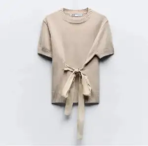 Superfin beige stickad topp från Zara med korta ärmar och snygg knytning i midjan. Rund halsringning och ribbade detaljer vid ärmslut och nederkant. Perfekt att styla med jeans eller kjol för en chill och trendig look.