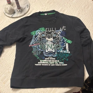 Svart sweatshirt från Kenzo med tiger - Cool svart sweatshirt från Kenzo med stort broderat tigerhuvud och färgglada detaljer på bröstet. Tröjan har rund hals, långa ärmar och ribbade muddar. Perfekt statement-plagg för dig som gillar streetstyle och unika prints.