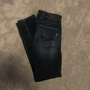 Replay Anbass svarta slim jeans 32 - Snygga svarta Replay Anbass jeans i slim fit med klassisk femficksdesign. Jeansen har en mörk tvätt med lätt slitning och subtila detaljer på bakfickan. Pris kan diskuteras vid snabb affär!