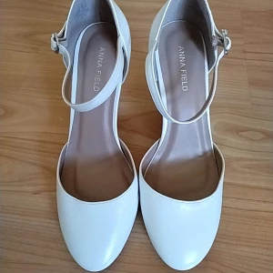 Vita pumps med rem från Anna Field - Stilrena vita pumps från Anna Field med rund tå och smal rem runt vristen. Skorna har en låg klack och är tillverkade i syntetmaterial med en slät finish. Perfekta för dig som vill ha en klassisk och elegant look.