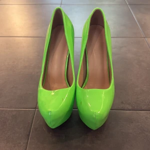 Neongröna platåpumps med 14cm hög klack - Säljer ett par riktigt snygga neongröna pumps med platåsula och 14cm hög klack. Skorna har rund tå och är tillverkade i glansigt syntetmaterial som verkligen sticker ut. Perfekta för dig som vill ha en färgklick till outfiten!