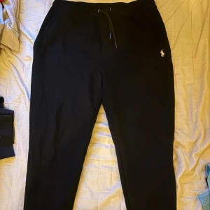 Svarta mjukisbyxor från Ralph Lauren - Svarta mjukisbyxor från Ralph Lauren med klassisk vit broderad logga på vänster höft. Byxorna har dragsko i midjan och är tillverkade i mjukt bomullsmaterial. Perfekta för chill dagar eller när du vill vara bekväm men ändå se stilren ut.