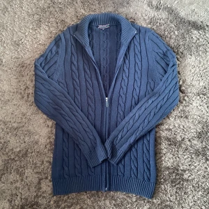 Mörkblå kabelstickad kofta Felix Hardy - Mörkblå kabelstickad kofta från Felix Hardy i storlek M. Koftan har hel dragkedja framtill, ribbade muddar och hög krage. Perfekt för lager-på-lager och chill höst- eller vinterstil.