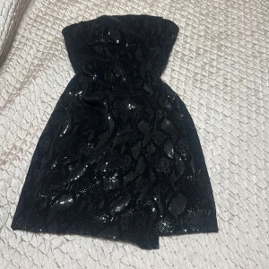 Svart paljettklänning från Zara - Säljer en svart, glittrig tubklänning från Zara. Klänningen är kort och täckt av paljetter som ger en snygg glansig effekt. Den är axelbandslös och har en figurnära passform som framhäver siluetten. Perfekt för dig som vill sticka ut.