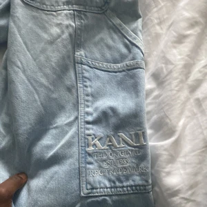 Ljusblå baggy jeans från Karl Kani - Säljer ett par ljusblå baggy jeans från Karl Kani med broderad logga på benet och bakficka. Jeansen har flera stora fickor och klassisk läderpatch i midjan. Perfekta för dig som gillar streetwear och vill sticka ut med en avslappnad stil.