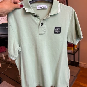 Grön pikétröja från Stone Island - Snygg ljusgrön pikétröja från Stone Island med klassisk krage, två knappar och logotyp på bröstet. Tröjan har korta ärmar och vita detaljer på kragen och ärmsluten. Perfekt för en clean och sportig stil. Pris går att diskuteras!