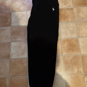 Svarta mjukisbyxor från Ralph Lauren - Svarta mjukisbyxor från Ralph Lauren med klassisk vit broderad logga på vänster höft. Byxorna har dragsko i midjan, muddar vid bensluten och en bakficka med dragkedja. Perfekta för chill eller träning.