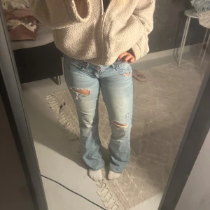 Ljusblå bootcut jeans med slitningar - Säljer ett par ljusblå jeans med bootcut-modell och snygga slitningar på låren och knäna. Köpte dom på vinted och tjejen innan har själv sytt de lågmidjade därmed förekommer ett litet hål på sista bilden men går lätt att ordna!!!.