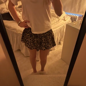 Leopardmönstrad kortkjol - Säljer en snygg kortkjol med leopardmönster. Kjolen har en lätt utställd passform och resår i midjan för extra komfort. Färgerna går i brunt, svart och beige vilket gör den enkel att matcha med olika toppar. Perfekt för dig som vill sticka ut lite extra.