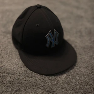 New Era Yankees keps 59FIFTY svart/blå - Säljer en svart New Era 59FIFTY Yankees keps med blått NY-logga framtill. Skärmen har ett unikt blått och vitt tie-dye mönster på undersidan. Klassisk passform och officiell MLB On-Field modell. Perfekt för dig som vill sticka ut med en snygg detalj.