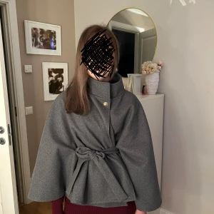 Grå kappa (Gina) - Snygg grå cape-kappa med hög krage och knytbälte i midjan. Helt ny använd 1 gång