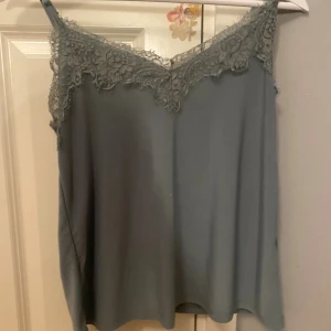 Grå linnetopp med spets från Amisu - Supersnygg grå linnetopp från Amisu i storlek XS. Toppen har tunna axelband och v-ringning med fina spetsdetaljer längs kanten. Perfekt för lager på lager eller som statement-piece till jeans eller kjol.