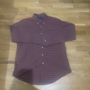 Rutig röd skjorta från Ralph Lauren - Snygg rutig skjorta från Ralph Lauren i rött, grönt och vitt. Skjortan har klassisk button-down krage, långa ärmar och vita knappar framtill. Custom fit-modell i mjuk bomull, perfekt för dig som gillar en tidlös och stilren look.