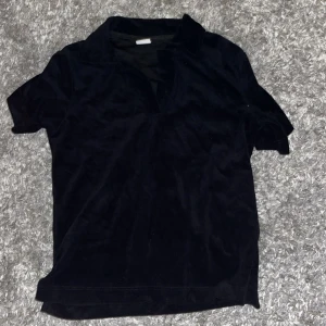 Svart pikétröja i sammet från Stories - Svart pikétröja från Stories i mjuk sammet. Klassisk krage och korta ärmar ger en clean look. Perfekt för dig som gillar stilrena vibes med en twist av lyxigt material. Nypris 250