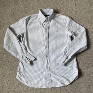 Ralph Lauren skjorta - Klassisk skjorta från Polo Ralph Lauren med smala blå och vita ränder, broderad logga på bröstet och knappar framtill. Den är i mycket fint skick med minimala tecken på användning! Skriv gärna vid minsta lilla fråga🌟