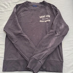 Lila sweatshirt från Gant - Säljer en lila sweatshirt från Gant med tryck 'GANT USA EST. 1949 NEW HAVEN' på bröstet. Tröjan har rund halsringning, långa ärmar och ribbade muddar vid ärmslut och nederkant. Perfekt för en chill och avslappnad stil.