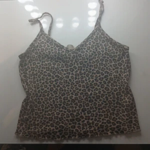 Leopardmönstrad linnetopp från H&M - Säljer en snygg leopardmönstrad linnetopp från H&M i beige och bruna toner. Toppen har smala axelband med knyt och ärmlös design. Perfekt för dig som gillar djurmönster och vill ha en trendig och bekväm topp till sommaren.