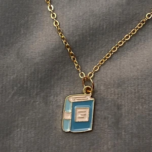 Halsband bok guld imitation  - Sött halsband med en berlock i form av en blå bok. Boken är ca 1 x 1,4 cm. Trädd på kedja i guldimitation som är justerbar 40-45 cm. Perfekt för den som älskar böcker! 