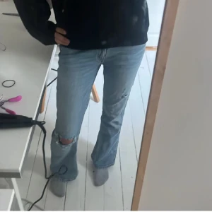 Ljusblå bootcut gina tricot jeans - Säljer ett par ljusblå gina jeans med bootcut passform och låg midja. Jeansen har slitningar och hål på ena knät för en cool, avslappnad look. Klassisk femficksmodell i mjukt denimtyg, perfekt till sneakers eller boots.