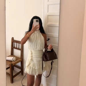  Ivy dress från Feeling Friday - Supersöt ljus kort klänning med halterneck och volanger i flera lager. Klänningen har markerad midja, omlott-detalj i sidan och är ärmlös. Perfekt för sommarens alla tillfällen och ger en romantisk vibe. Slutsålt på hemsidan. Använt en gång 