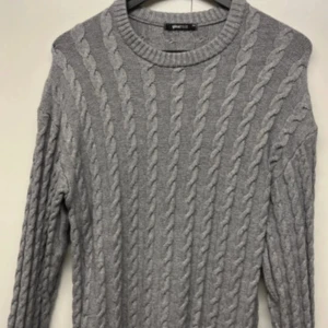 Grå kabelstickad tröja Gina Tricot XS - Kabelstickad grå tröja från Gina Tricot i storlek XS. Tröjan har rund halsringning, lång ärm och ett klassiskt flätmönster över hela plagget. Perfekt för lager-på-lager och chill höst- eller vinterstil.väldigt oversized. KNAPPT använd 