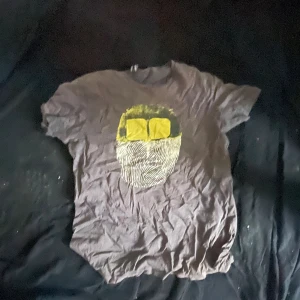 Svart t-shirt med gul print från Insight - Cool svart t-shirt från Insight med unik gul och vit print framtill som föreställer ett ansikte med glasögon. Klassisk passform och rund hals. Tillverkad i mjuk bomull, perfekt för en avslappnad streetstyle-look.