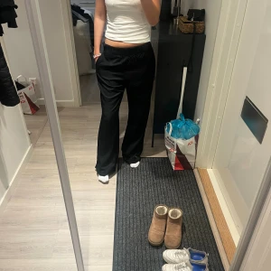 Svarta vida byxor med resårmidja - Svarta byxor med avslappnad passform och resår i midjan. Vida ben och mjukt, lätt material som ger en skön känsla. Perfekta för en chill och stilren look. Passar dig som gillar loose fit och enkel stil.