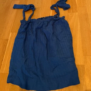 Blå topp  - Söt blå topp från H&M i storlek XS. Toppen har knytbara axelband och ett diskret rutigt strukturmönster i tyget. Perfekt för varma dagar och enkel att styla med sneakers eller sandaler.