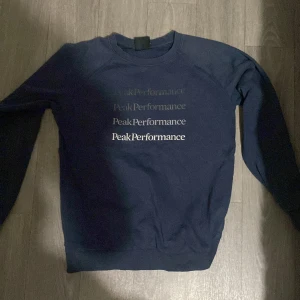 Mörkblå Peak Performance tröja - Snygg mörkblå sweatshirt från Peak Performance med tryckt logga i flera nyanser framtill. Tröjan har rund halsringning, långa ärmar och ribbade muddar. Perfekt för dig som gillar stilren och sportig look.