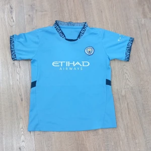 Manchester City Haaland 9 matchtröja - Snygg ljusblå Manchester City fotbollströja med Haaland 9 på ryggen och Etihad Airways-logga på bröstet. Kortärmad modell med mörkblå detaljer och klubbmärke på bröstet. Perfekt för dig som vill visa vilket lag du håller på.